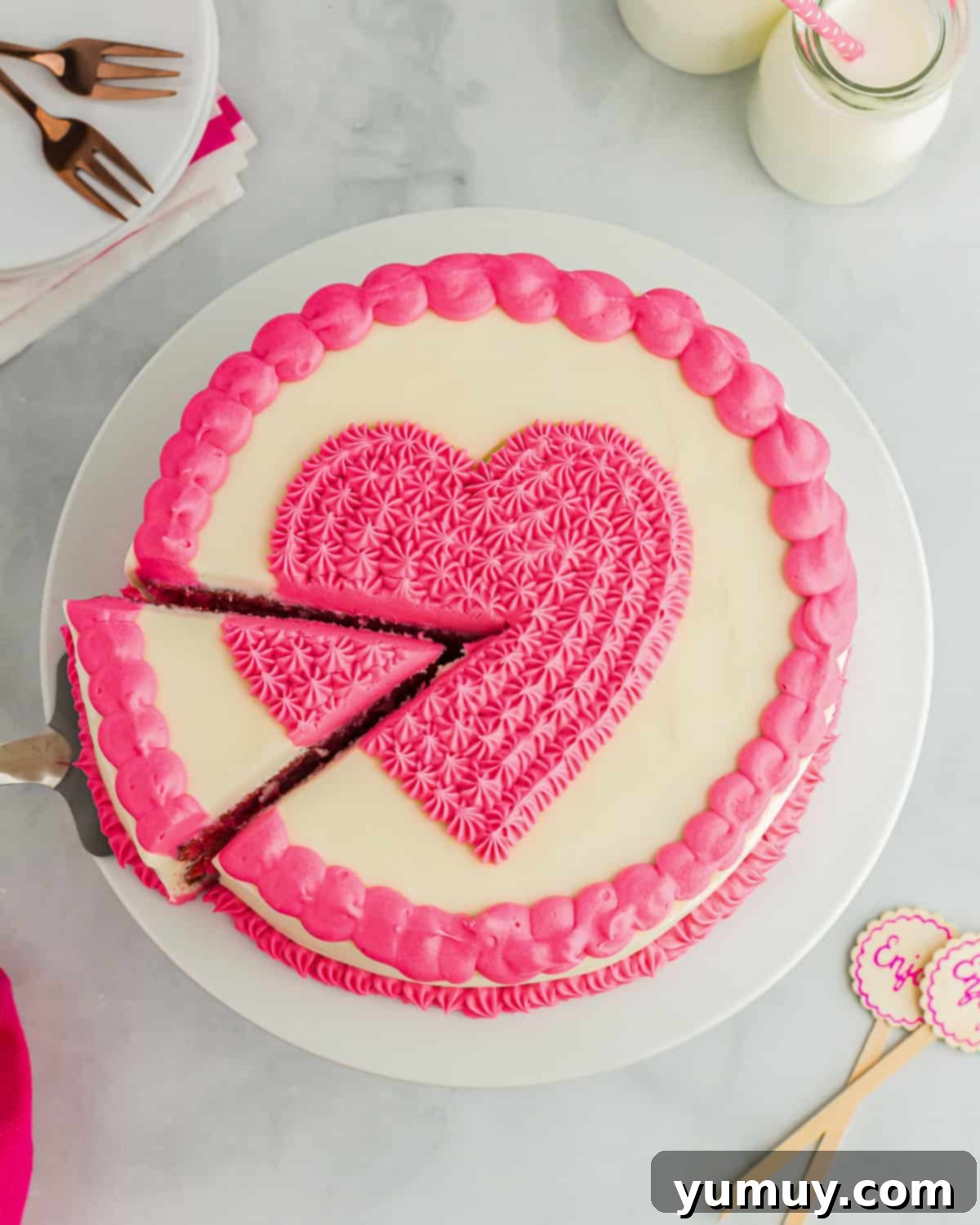 A cake server carefully removes a perfect slice of pink velvet cake from a freshly decorated whole cake, revealing its soft texture.