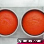 Two baked pink velvet cake layers in round cake pans, cooling after removal from the oven.