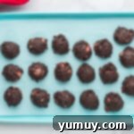 Scooping and shaping strawberry truffle mixture into perfectly round balls on a baking sheet.