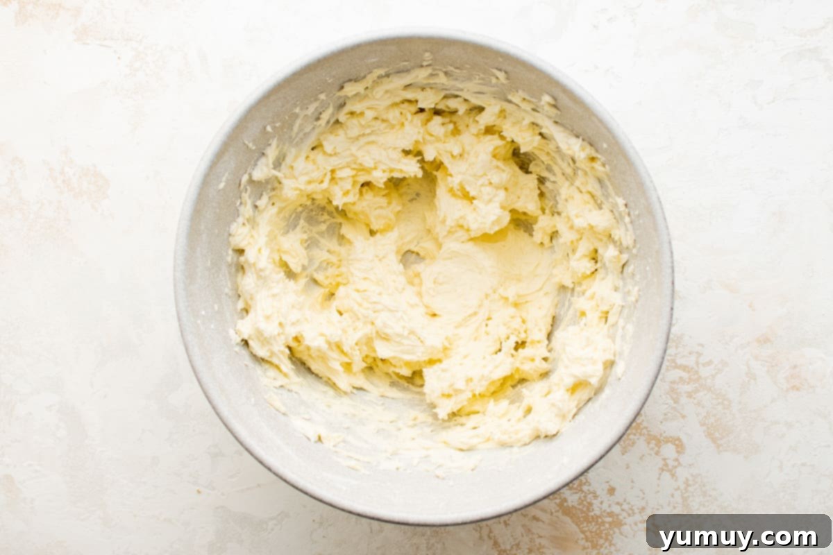 Tangy Lemon Curd Delights 11 Creamy butter being whipped in a bowl with a hand mixer, smoothly blended with egg and lemon extract on a pristine white surface.