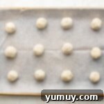 Tangy Lemon Curd Delights 7 Raw lemon cookie dough balls, perfectly coated in sparkling sugar and neatly arranged on a parchment-lined baking sheet.