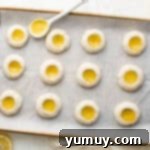 Tangy Lemon Curd Delights 9 Golden-edged lemon cookies fresh out of the oven, cooling on a baking sheet with a spoon nearby.