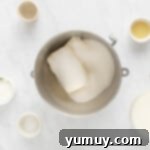 Cream cheese and powdered sugar being beaten together in a large mixing bowl with an electric mixer, forming a smooth, fluffy cheesecake base.
