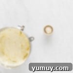 The fluffy, white whipped cream being gently folded into the cream cheese mixture in a metal bowl, creating a smooth, airy cheesecake filling.