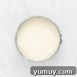 The smooth, creamy cheesecake filling poured evenly over the chilled crust in a springform pan, ready for chilling.