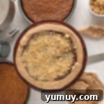 graham cracker crumbs sprinkled over chocolate ganache surrounded a chocolate frosting dam on a layer of graham cracker cake on a cake stand.