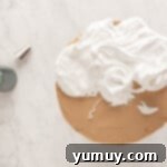 meringue being swirled over a frosted smores cake on a cake stand.