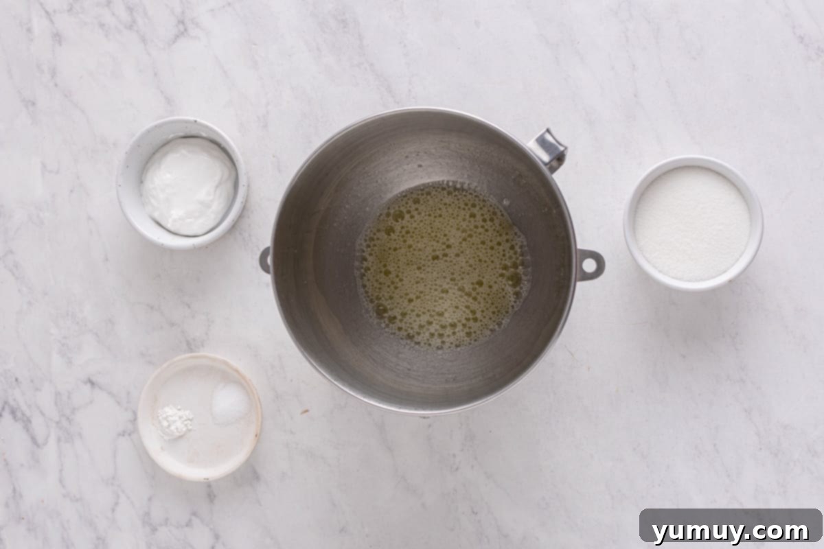 Foamy egg whites in a stainless steel mixing bowl, showing the initial microfoam stage.