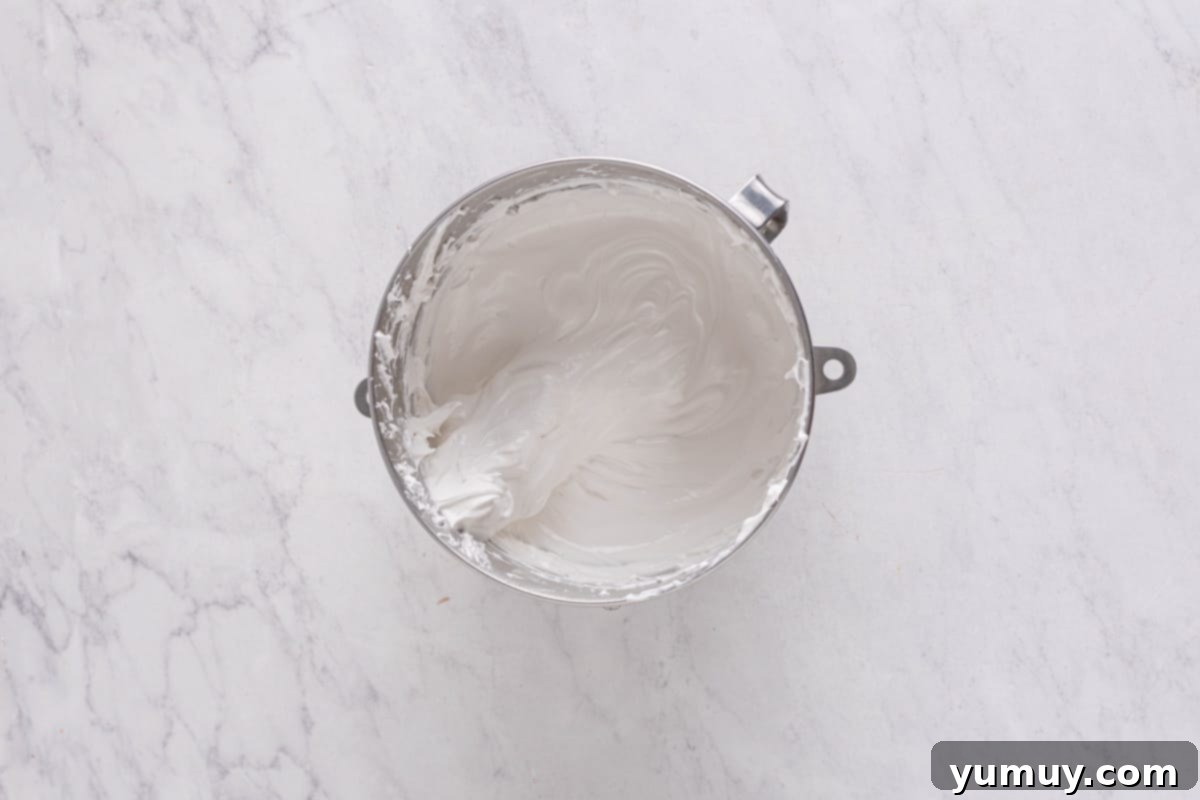 Perfectly whipped marshmallow meringue in a stainless steel mixing bowl, showing stiff peaks.
