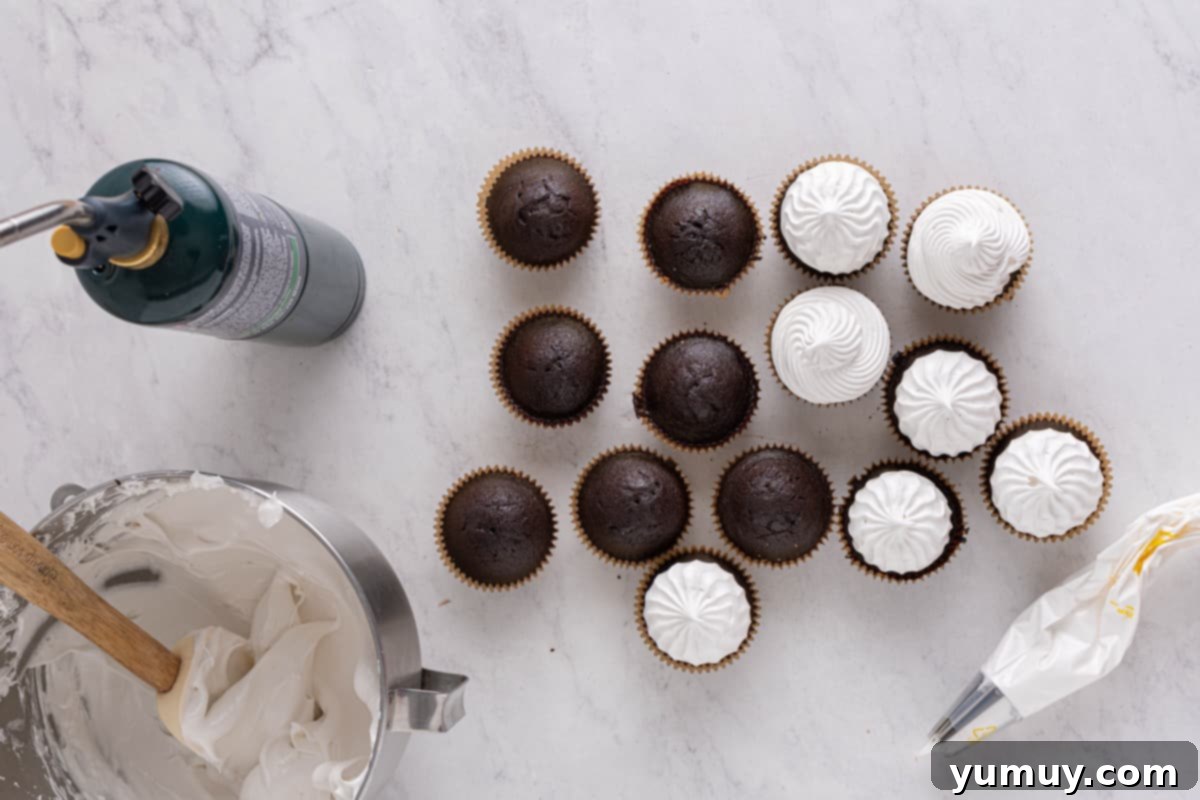 Overhead view of several chocolate cupcakes, some already frosted with elegant swirls of marshmallow meringue.