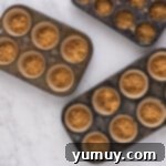 Graham cracker crust mixture pressed firmly into the wells of cupcake tins, ready for baking.