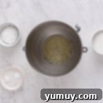 Foamy egg whites in a stainless steel mixing bowl, showing the initial microfoam stage.