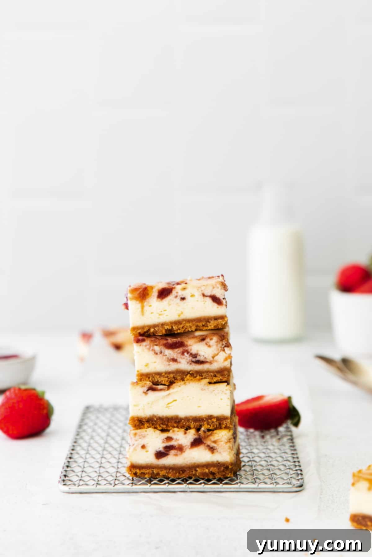 Luscious Strawberry Cheesecake Bars 3 Side view of four stacked strawberry cheesecake bars on a wire cooling rack, showing the distinct layers and strawberry swirls.