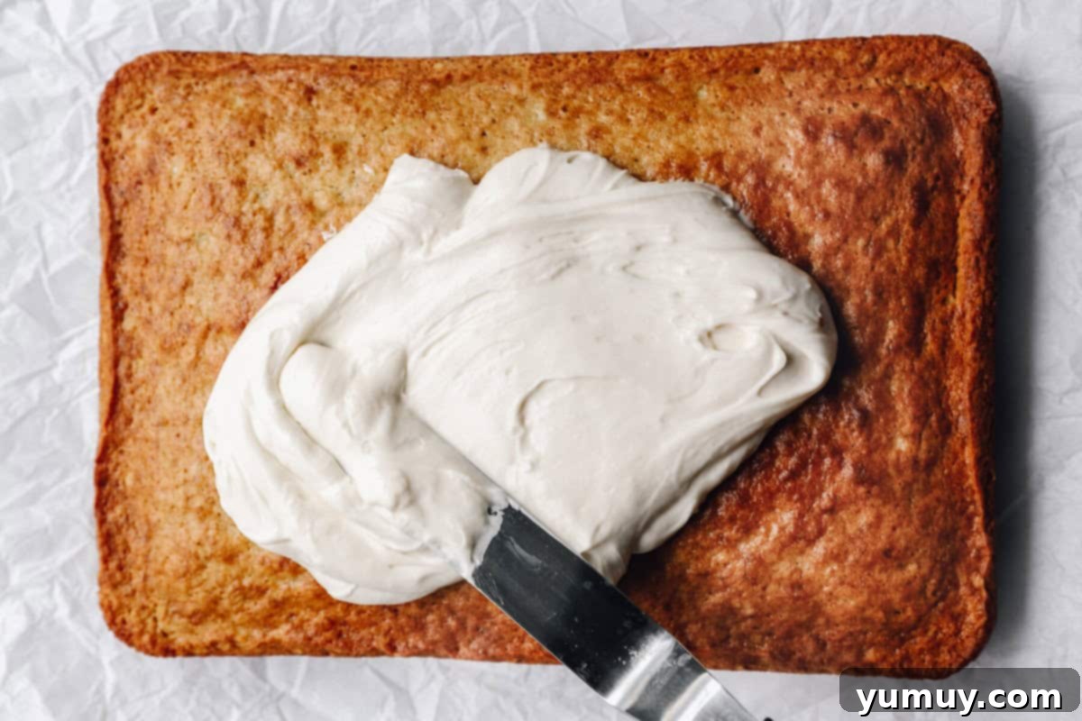 an offset spatula spreading cream cheese frosting over a baked banana cake.