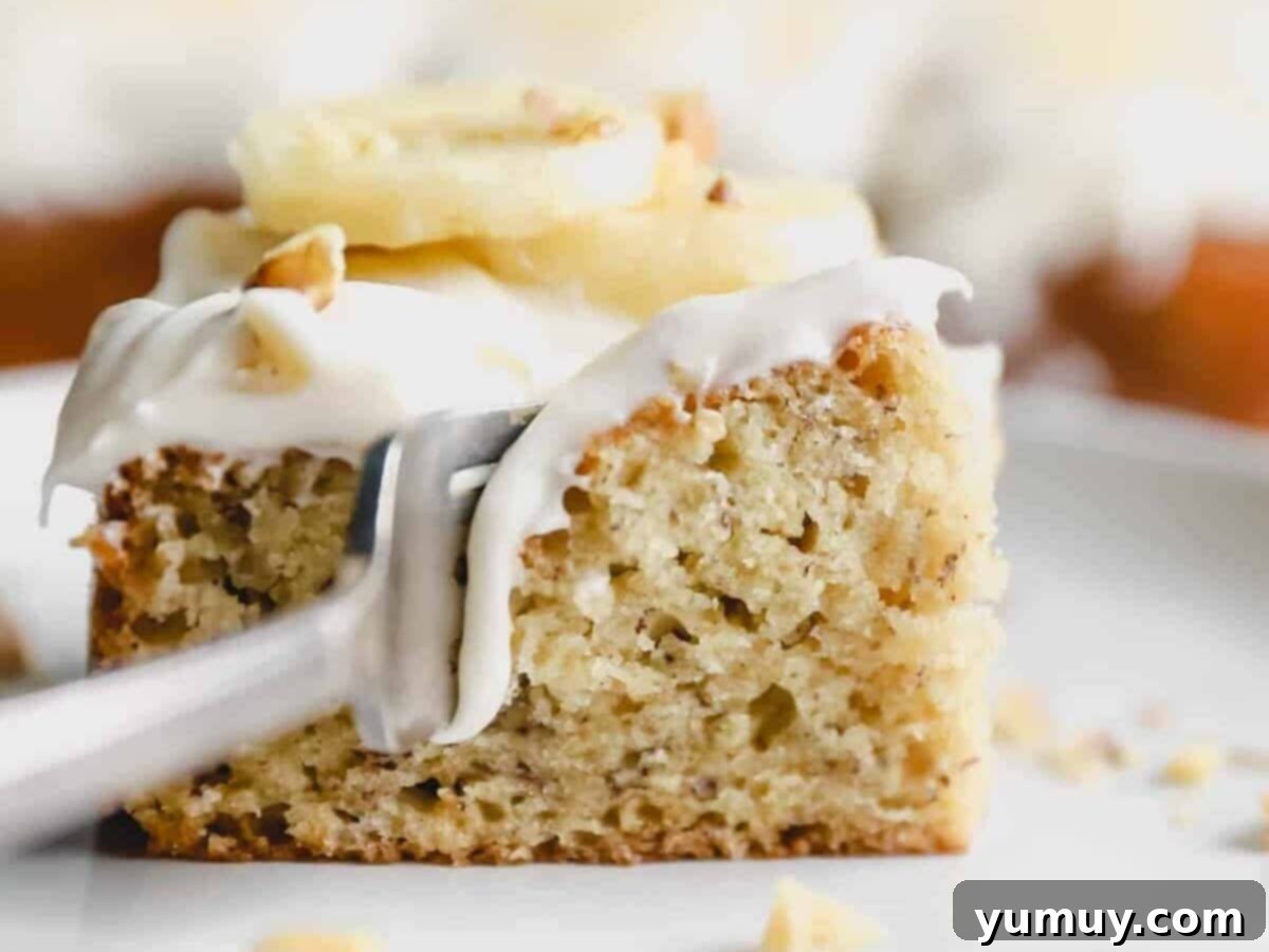 side view of a fork slicing into a slice of cake mix banana cake with cream cheese frosting on a white plate.