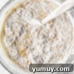 dry ingredients being folded into wet ingredients for banana cake in a glass bowl with a rubber spatula.
