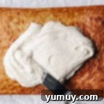 an offset spatula spreading cream cheese frosting over a baked banana cake.