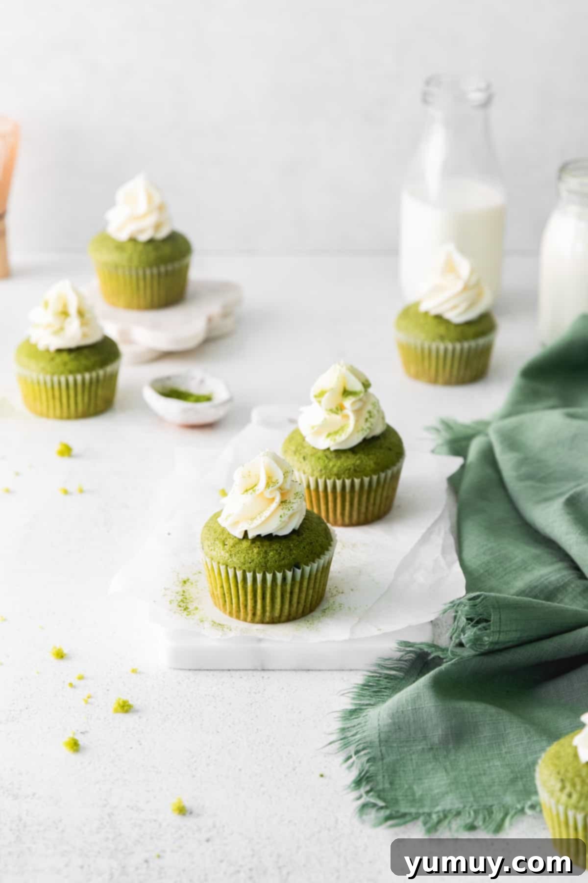 A close-up view of two frosted matcha cupcakes on parchment paper, highlighting their vibrant green color and elegant cream cheese frosting.