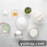 Overhead view of various ingredients for matcha cupcakes, neatly arranged in individual bowls on a kitchen counter.