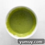 Vibrant green matcha cupcake batter in a pristine white mixing bowl, ready for baking.