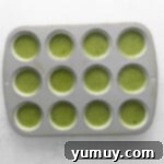 Bright green matcha cupcake batter neatly portioned into the wells of a 12-count cupcake tin, ready for the oven.