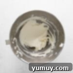 Smooth and fluffy cream cheese frosting filling a stainless steel mixing bowl, prepared for piping.