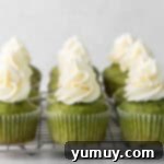 A side view of nine beautifully frosted matcha cupcakes arranged on a square wire rack, garnished with a sprinkle of matcha powder.