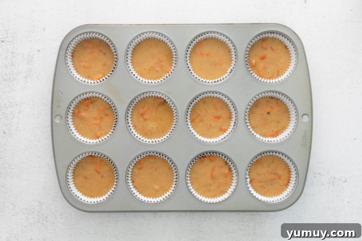 Cupcake batter carefully portioned into a 12-count cupcake tin with paper liners, ready for the oven.