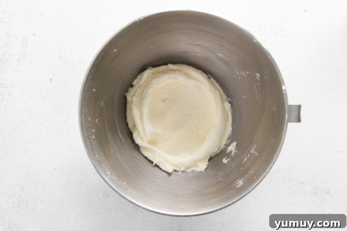 Creamy, white cream cheese frosting meticulously prepared in a stainless steel mixing bowl, showcasing its smooth and airy texture.