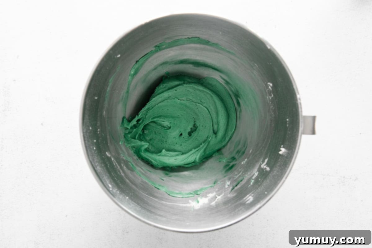 Vibrantly green-colored cream cheese frosting swirled beautifully in a stainless steel mixing bowl, ready for piping onto cupcakes.