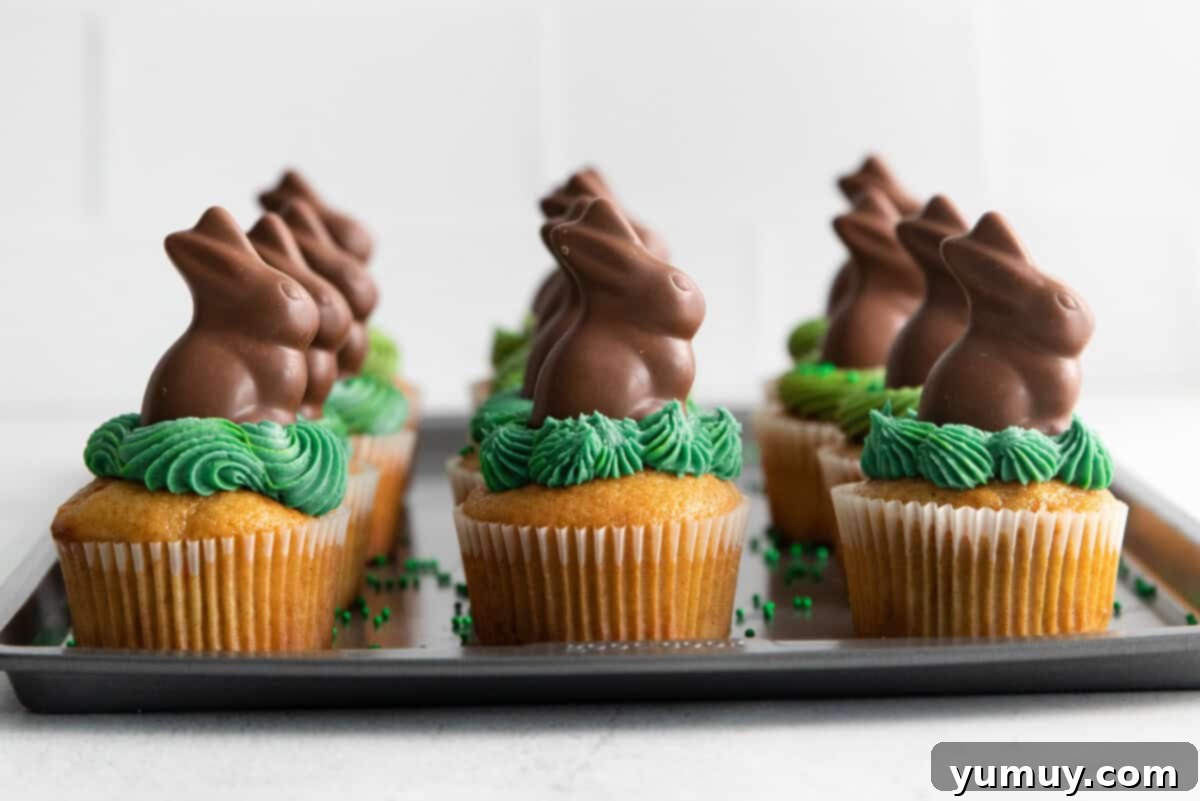 A baking tray filled with freshly frosted Easter bunny cupcakes, each adorned with a cute chocolate bunny, ready to be served.