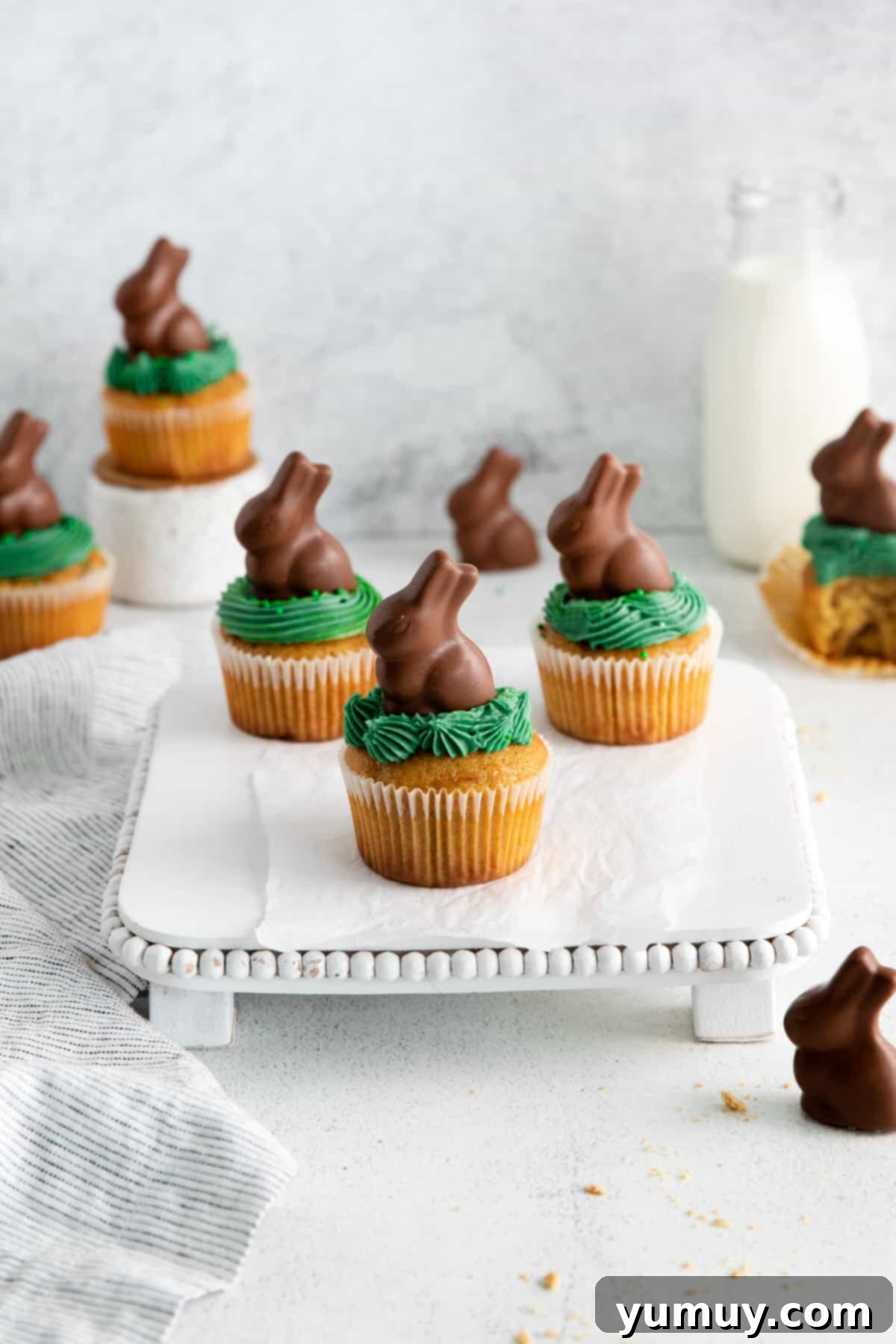 A three-quarters view of three charming Easter bunny cupcakes beautifully arranged on a square white cake stand.