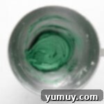 Vibrantly green-colored cream cheese frosting swirled in a stainless steel mixing bowl, ready for piping.