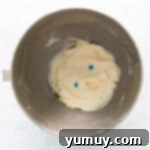 frosting for easter cupcakes in a stainless mixing bowl with 2 drops of blue food coloring on top