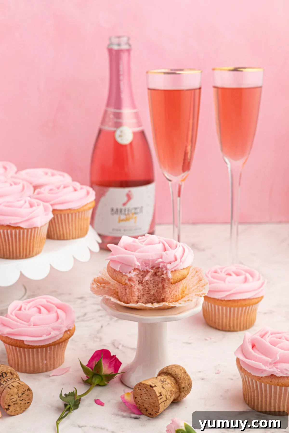 Side view of a bitten moscato cupcake on a cupcake stand in front of two glasses of pink moscato, highlighting its festive pink hue and soft texture.