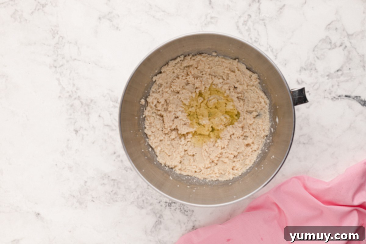 Room temperature eggs being added to creamed butter and sugar in a stainless steel mixing bowl, ready to be beaten.