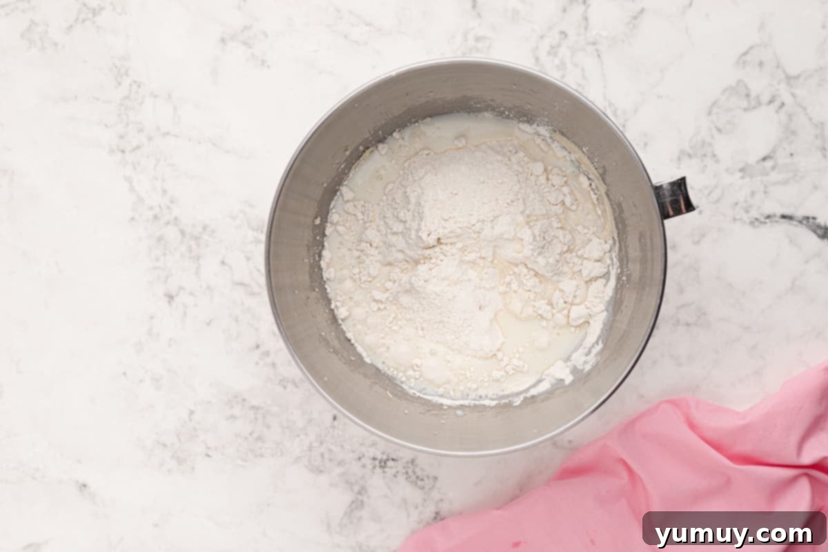 Dry ingredients, including flour and baking powder, being added alternately with milk to the wet batter in a stainless steel mixing bowl.
