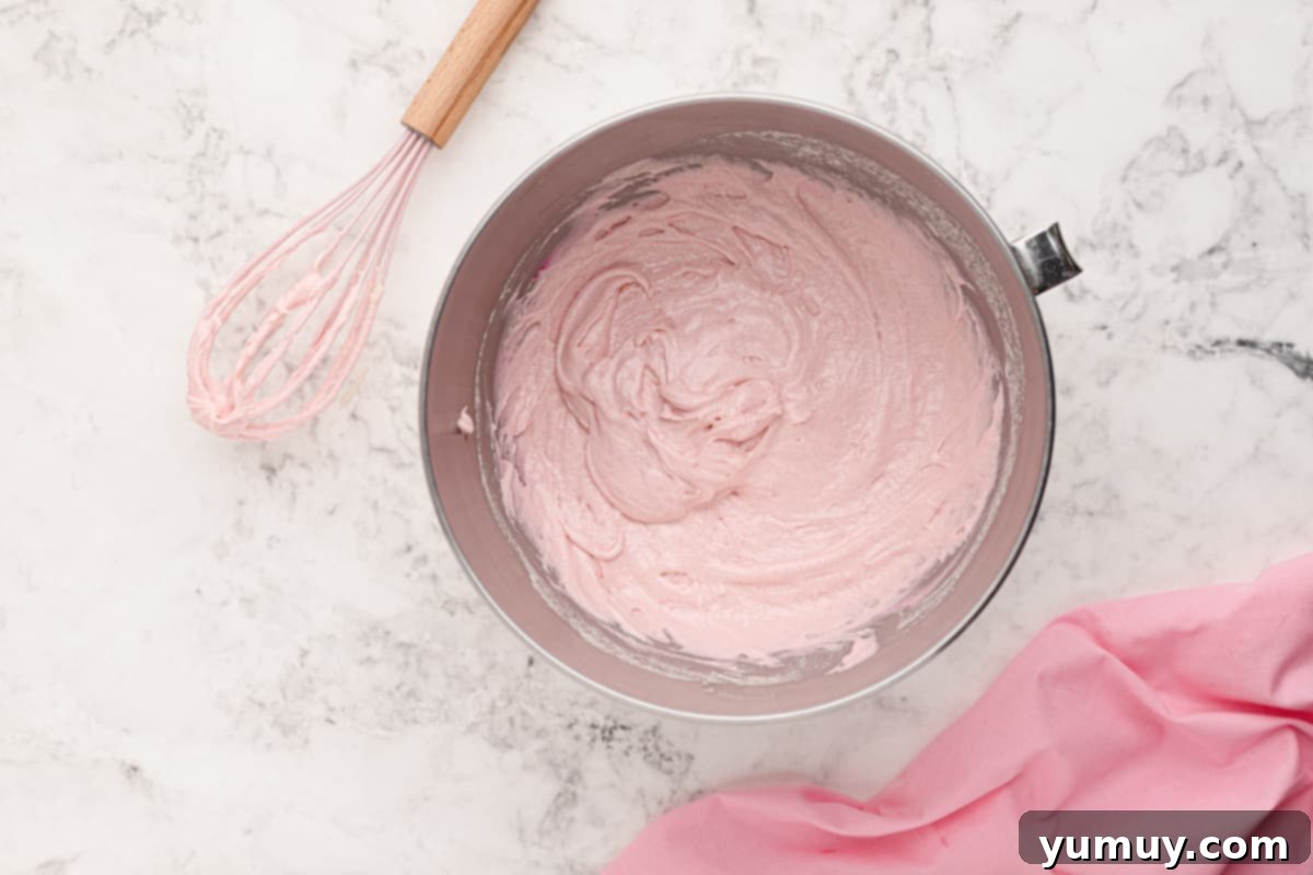 Pink moscato cupcake batter swirled in a stainless steel mixing bowl with a whisk, showcasing the beautiful pink hue.
