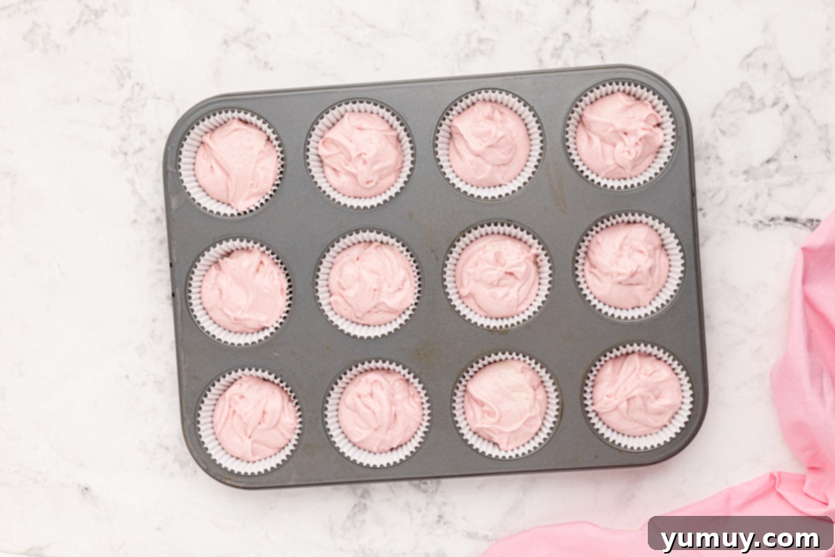 Moscato cupcake batter precisely poured into the wells of a 12-count cupcake tin, ready for baking.