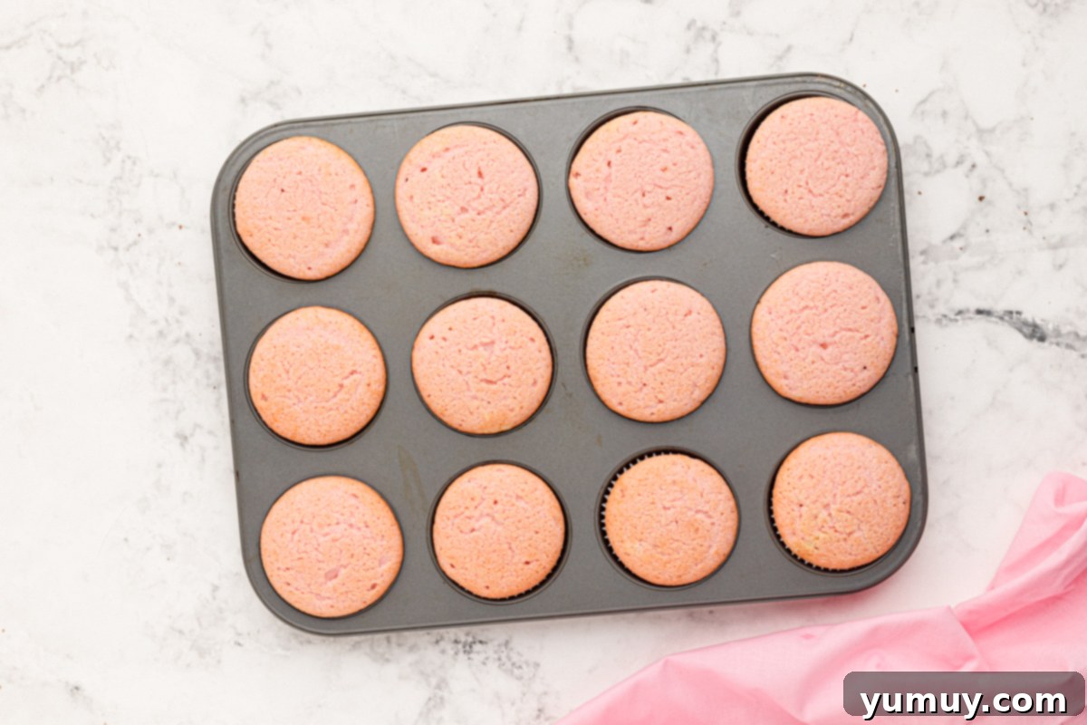 A tray of 12 freshly baked pink moscato cupcakes, golden and perfectly risen, cooling in a cupcake tin.