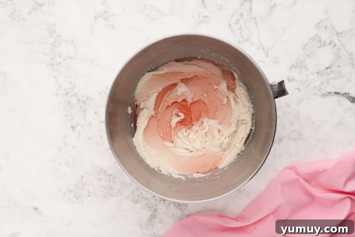 Pink Moscato wine being slowly added to a creamy frosting mixture in a stainless steel mixing bowl, creating a beautiful blush color.