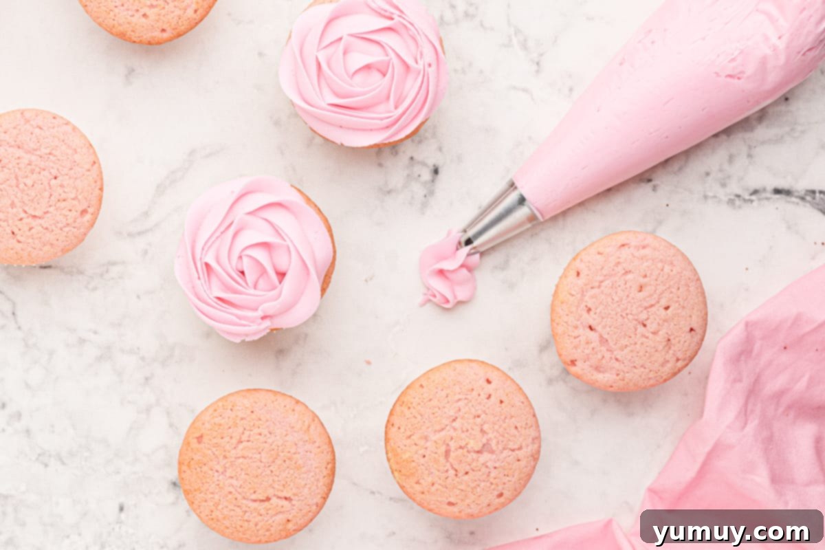 A collection of pink moscato cupcakes, some already frosted with elegant swirls, next to a piping bag filled with pink buttercream.