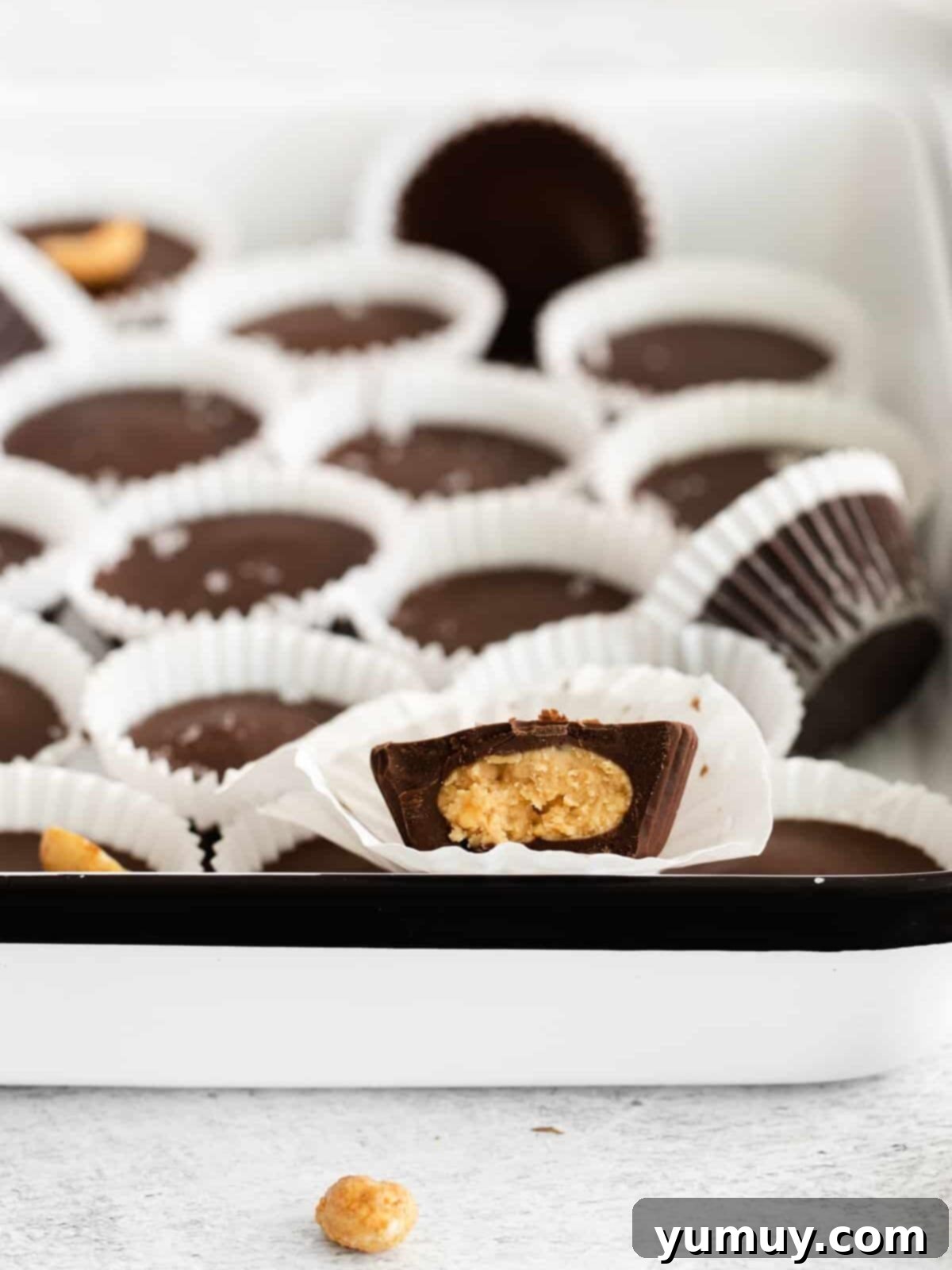 close up of a halved crunchy peanut butter cup in a paper liner, with more peanut butter cups in the background, showcasing the crunchy peanut filling.