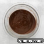 Chocolate sauce in a glass bowl on a white background, showing its melted consistency.