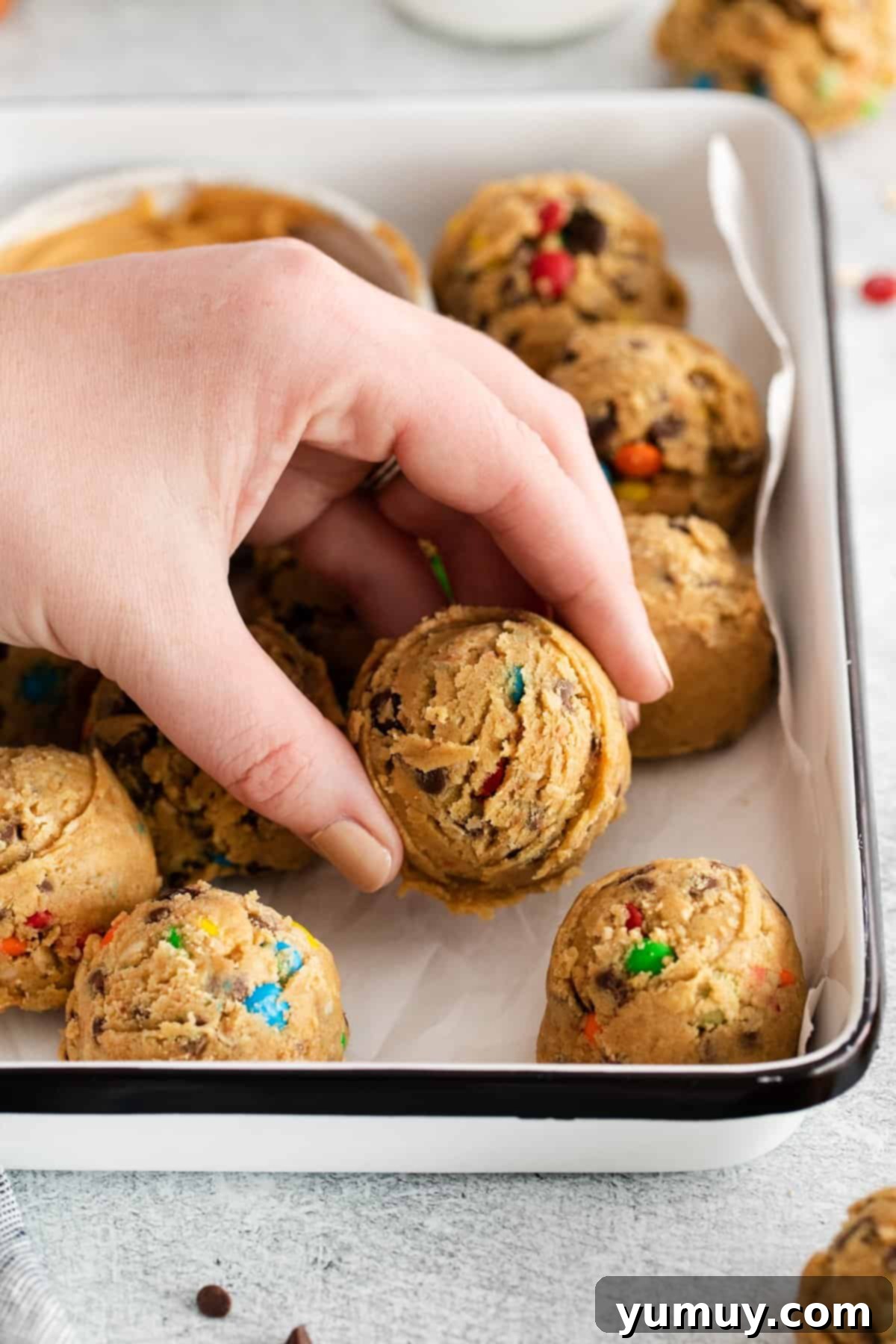 No-Bake Monster Cookie Dough 2 A hand grabbing a ball of edible monster cookie dough from a tray, showcasing its rich texture and colorful M&Ms.