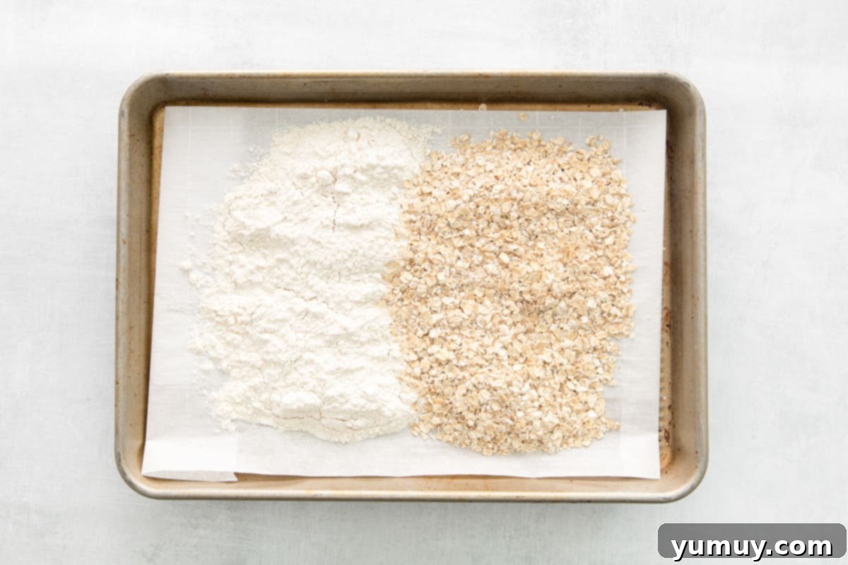 No-Bake Monster Cookie Dough 6 Quick oats and all-purpose flour spread thinly on a baking sheet, ready for heat treatment.