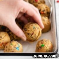 No-Bake Monster Cookie Dough 4 A hand reaching into a baking pan full of cookie dough balls, highlighting the delicious texture.