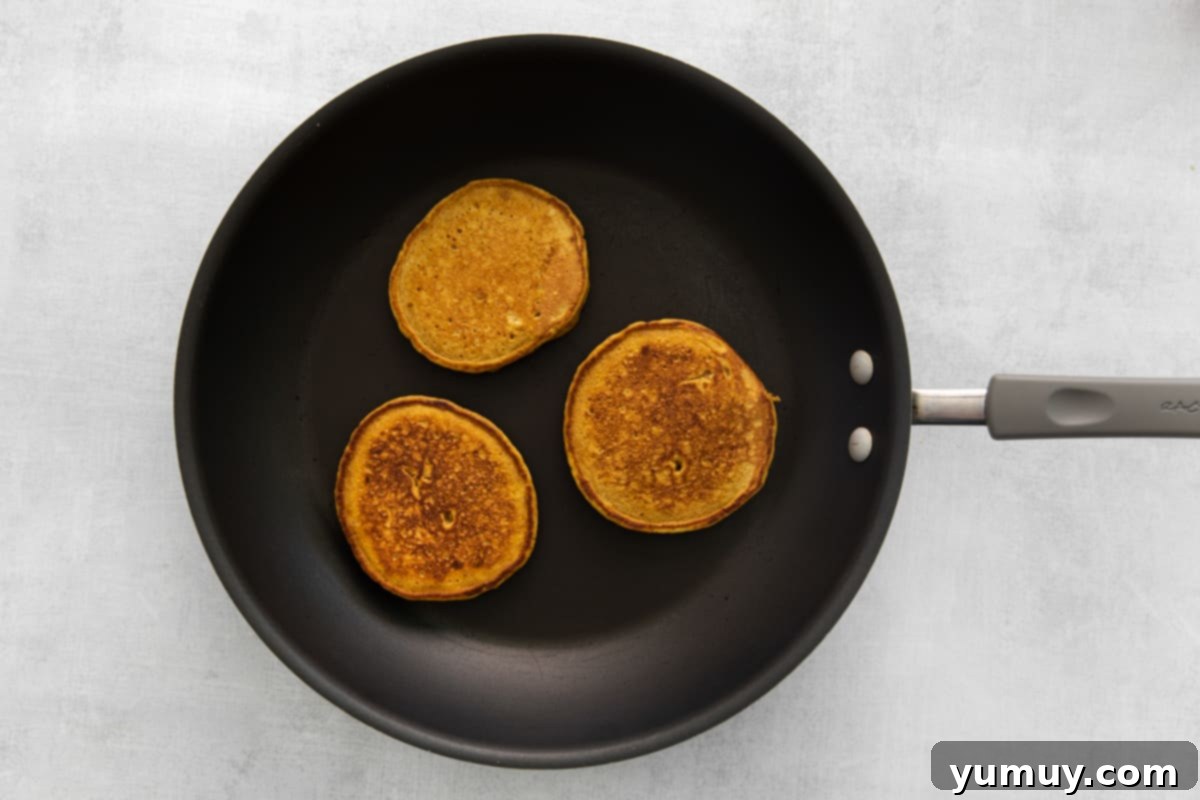 A pumpkin pancake cooking on a griddle, with visible bubbles on the surface.