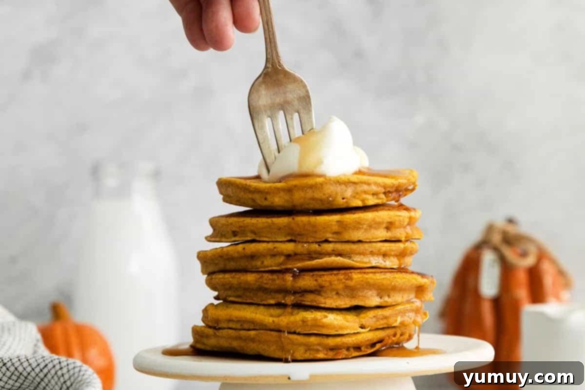 A fork piercing a stack of whipped cream-topped pumpkin pancakes, highlighting their fluffy texture.