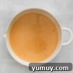 A bowl containing mixed wet ingredients for pumpkin pancakes, ready for dry ingredients.